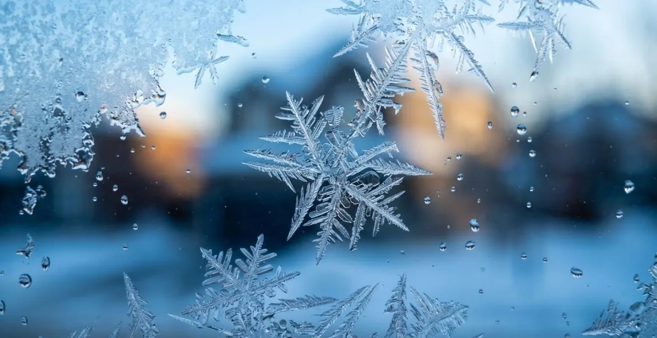 Cristaux de givre formant des motifs géométriques sur une vitre avec gouttes d'eau en dégel, évoquant les cycles thermiques hivernaux québécois